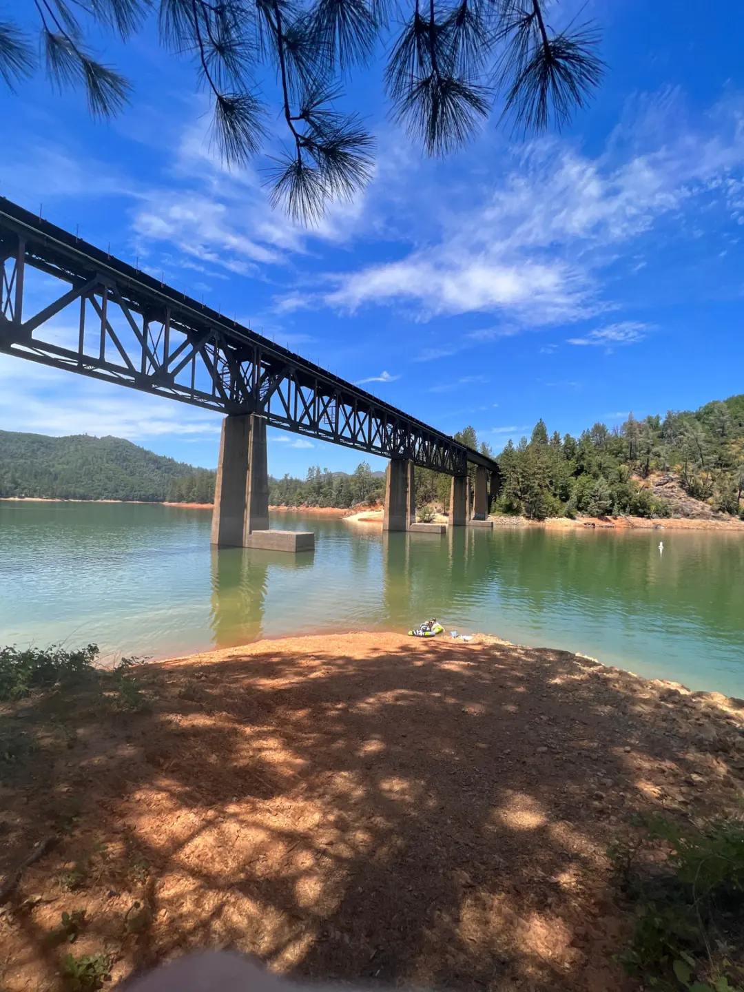 The steel railroad trestle crossing the Lower Salt Creek arm of Shasta Lake above a red dirt shoreline