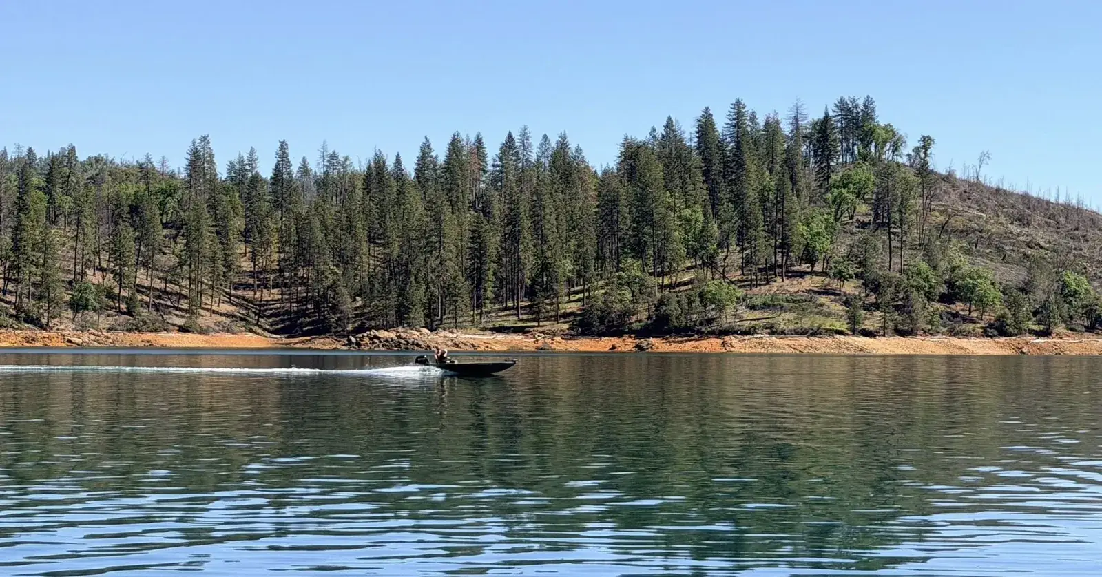 Small boat passing a forested point on Shasta Lake in the fall