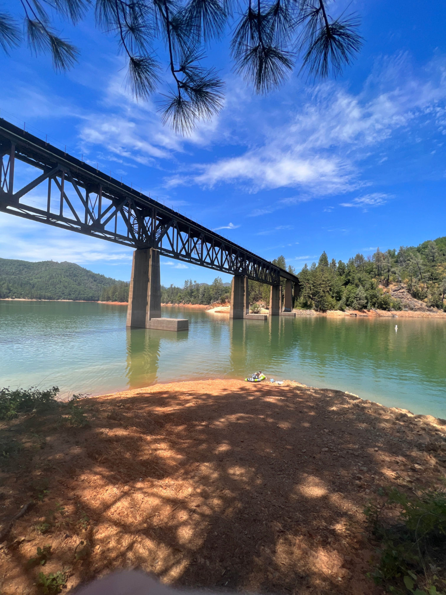 The steel railroad trestle crossing the Lower Salt Creek arm of Shasta Lake above a red dirt shoreline